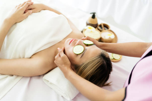 istock Relaxing young Asian woman lying down and using sliced cucumbers on her closing eyes on massage beds while receiving a massage from a therapist at an Asian luxury spa salon and a wellness center. 1659115437
