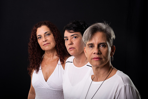 Portrait of three beautiful women, lesbians, musician friends and happy in a row posing for the camera. Studio shot against black background.