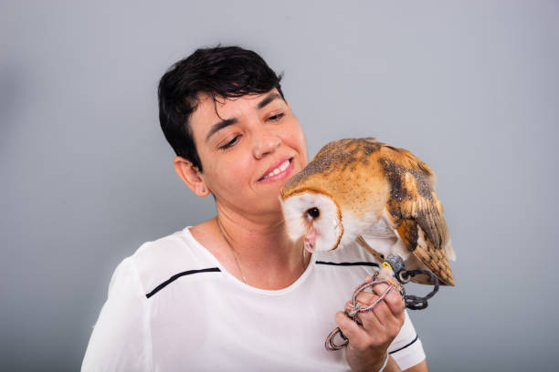 A woman lovingly looking at her owl. Wild animal. Against gray background.