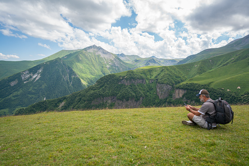 Traveling man using his phone against the Caucasus Mountains view on a cloudy summer day in Kazbegi, Georgia