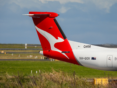 A Qantas De Havilland Canada Dash 8-200 plane, registration VH-QOV, waiting to enter the main runway of Sydney Kingsford-Smith Airport for departure as flight QF2225 to Wagga Wagga.  This image was taken from Nigel Love Bridge, Mascot on a sunny and windy afternoon on 2 September 2023.