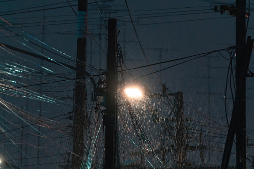 Rainstorm falling with street lamp light and messy electric pole and wires connected in the night on suburban