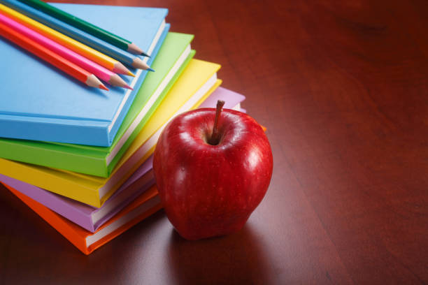 A stack of books with some pencils and an apple.