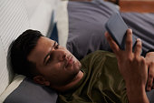 Young man in t-shirt looking through online news or video in smartphone