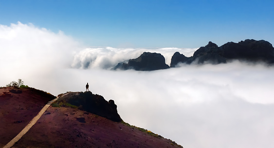 Young hiker standing on a cliff above the clouds - Backpacking on top of a mountain and trekking - Adventure travel concept