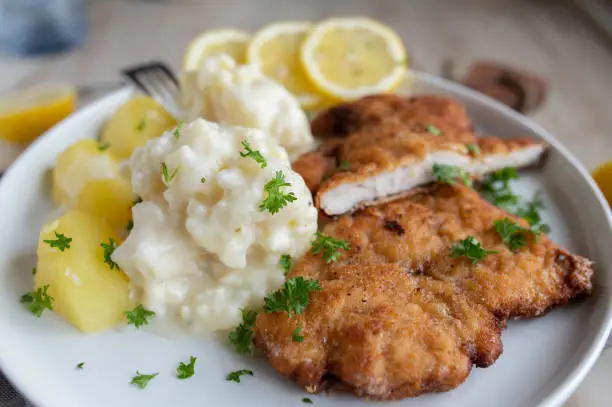 Homemade german dish with creamy cauliflower in a delicious bechamel sauce. Served with breaded pork schnitzel and boiled potatoes on a plate. Closeup, front view