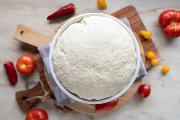 Homemade fresh raw and risen pizza dough with ingredients background. Closeup, Top view with copy space.