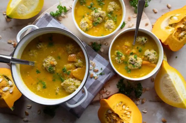 Delicious homemade pumpkin soup with pork meatballs. Served ready to eat on a table in pot and in bowls with spoon. Top view