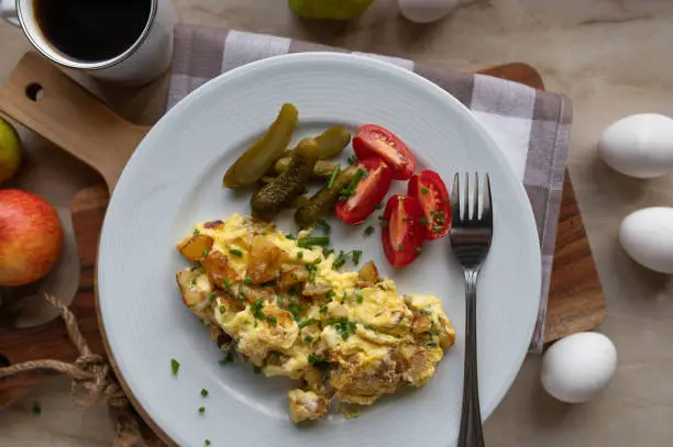 Traditional german breakfast, lunch or dinner with fresh fried potatoes, scrambled eggs. Served with sliced pickles and tomatoes on a plate. Top view