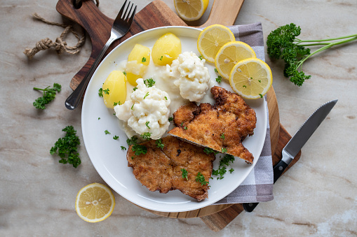 Homemade traditional german dish with a fresh pan fried and breaded pork schnitzel. Served with cooked cauliflower, bechamel sauce and potatoes on a plate. Top view with copy space