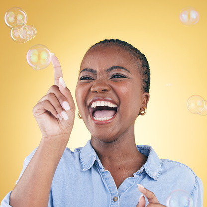 Excited, laugh and black woman on yellow background with bubbles for happiness, joy and have fun. Happy, smile and isolated African person in studio pop soap bubble for playful, magic and aesthetic