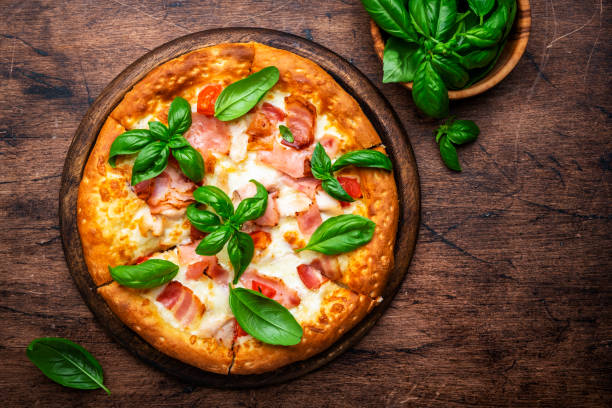istock Hot pizza with ham, pancetta, mozzarella cheese, tomato sauce and green basil, rustic wooden table background, top view 1659169645