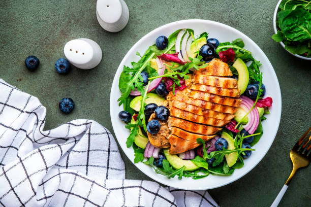 istock Delicious salad with blueberries, grilled chicken, avocado, red onion, walnuts, arugula and mixed herbs, green table background, top view 1659170142