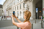 Young woman taking pictures with mobile phone while exploring the city of Vienna