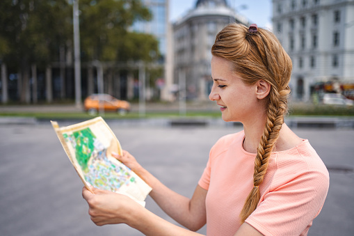 A beautiful female tourist in France. She is holding a large city map, checking out where to go next.