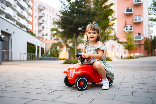 Portrait of a little girl outdoors sitting on a toy car