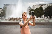 Young woman taking pictures with mobile phone while exploring the city of Vienna