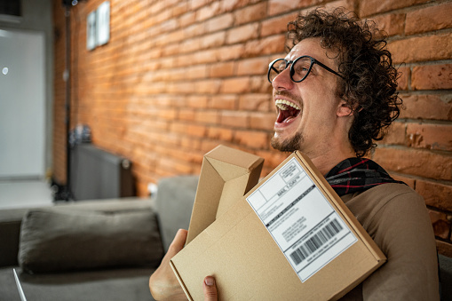 A happy white guy just received a package he ordered online. His excited face reflects excitement as he holds the package in his hands