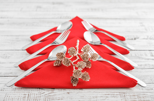 Red napkins in the shape of a Christmas tree with forks and spoons on wooden background closeup