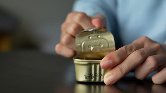 Cropped view focusing on a woman as she opens a can of mackerel in olive oil