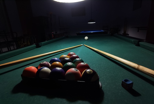 A billiard table in a dimly lit room, with snooker balls and cues arranged for a game