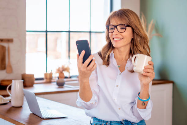 istock Attractive woman standing in the kitchen at home and using smartphone 1659281940