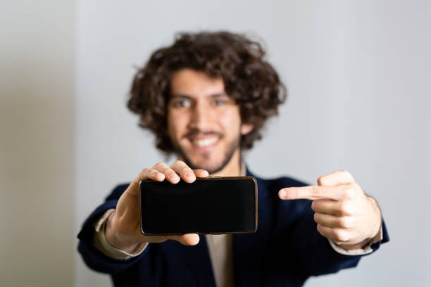 istock Young man with smartphone in hand pointing at black screen with finger 1659328109