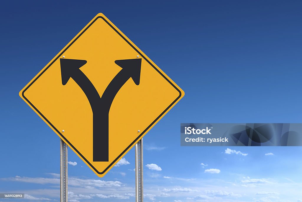 Choice or Division Ahead Road Sign Post on Blue Sky An informational traffic sign over a blue sky showing a division of directions - choice or decision - a clipping path is included to separate sign from bkg. Sign positioned to the left of the frame allowing for plenty of copy space. Road Sign Stock Photo