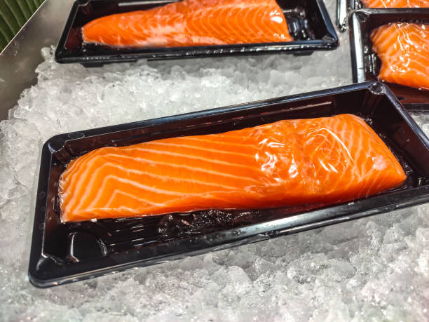 les parties du corps du saumon sont placées à l’intérieur d’un plateau en plastique sur des morceaux de glace pilée vendus dans les supermarchés. - freshness seafood crushed ice salmon photos et images de collection