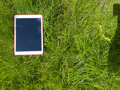 Top view shot of a modern digital tablet in green grass outdoors