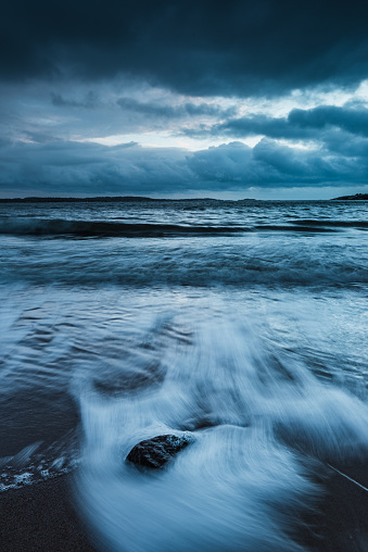 Serenity on a Swedish beach: waves, rocks, cloud-filled sky, and endless ocean horizon.