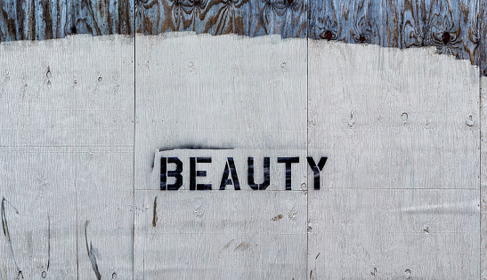 The black letters BEAUTY stenciled on an old, worn painted plywood wall.