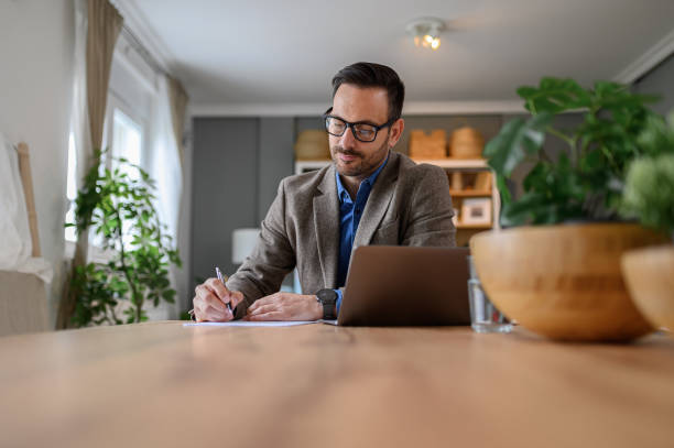 istock Focused young elegant businessman signing documents while working over laptop on desk at home office 1659397748