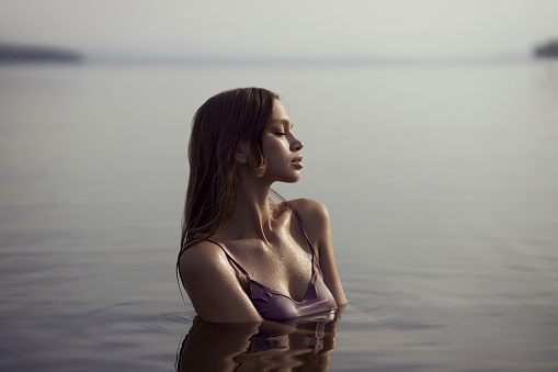 Beautiful woman meets sunset sitting in lake, perfect body, wet hair. Vacation relax by the water
