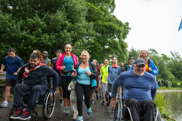 Running Together In The Rain A wide angle view of a group of people who are taking part in a fun run in Leazes Park in Newcastle upon Tyne ion the North East of England. They are all enjoying themselves despite the rainy weather. The race is open and fully inclusive of ages and abilities. It is also dog friendly. The two men setting the pace and leading are wheelchair users. Volunteering Mental Health stock pictures, royalty-free photos & images