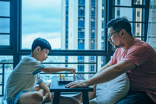 A father and his son are playing chess at home