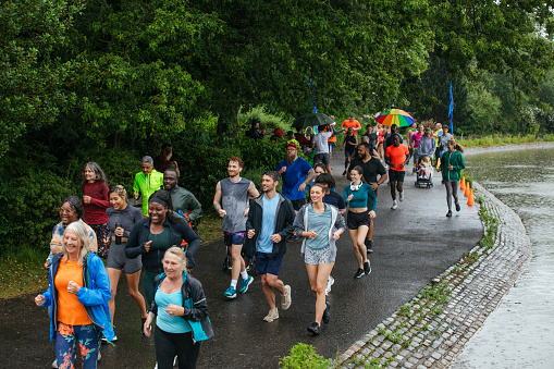 A high angle view of a group of run participants who are taking part in a park run in Leazes Park in Newcastle upon Tyne in the North East of England. They are running in the rain along the lakeside. The race is open to people of all ages and abilities and is also dog friendly.
