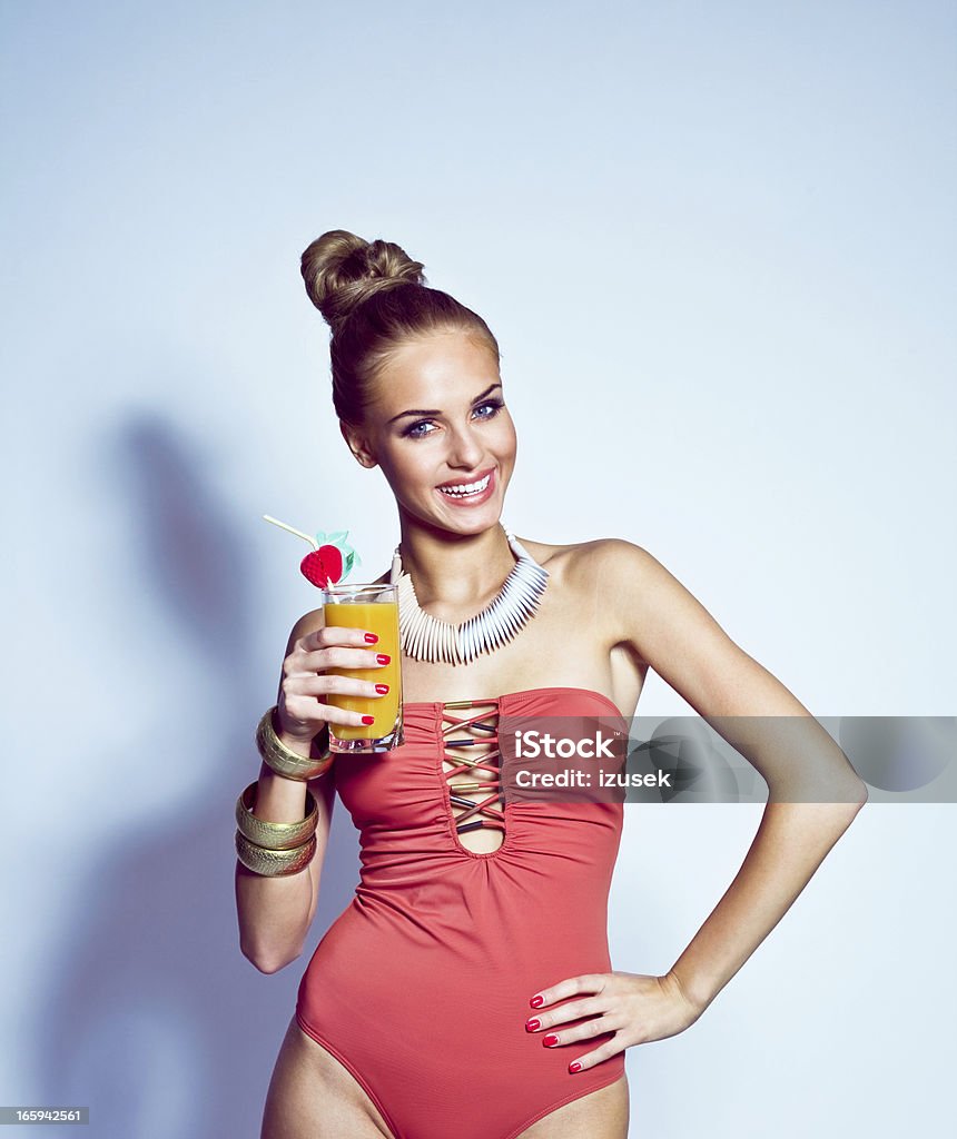 Glamour portrait of woman holding a tropical drink Beautiful young blond woman wearing pink holding glass with orange drink. Studio shoot, blue background. Summer portrait. Cocktail Stock Photo