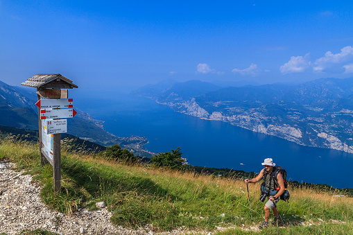 Hiker with photographing equipment on Monte Baldo, a mountain in the Italian Alps with a ridge that stretches for 40 km parallel to Lake Garda. It reaches the maximum elevation of 2,218 m with the Valdritta, and the minimum elevation of 65 m on Lake Garda, the largest Italian lake. 