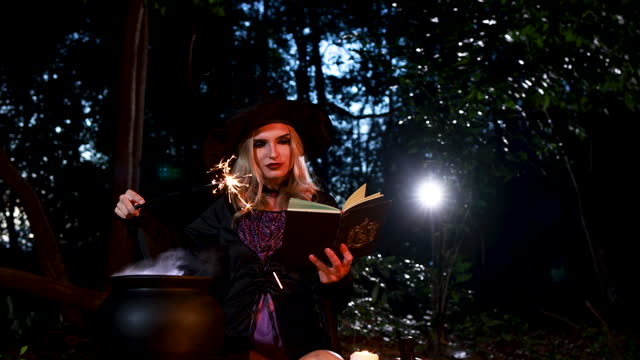 A young witch casting a magic spell in a Halloween ritual with a sparkle wand and white smoke effect in the forest.