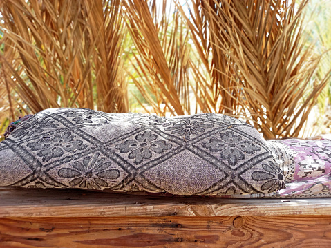 Berber chill out with fabric cushions on wood and a background of natural dry palm branches. Relaxation and Arab culture.