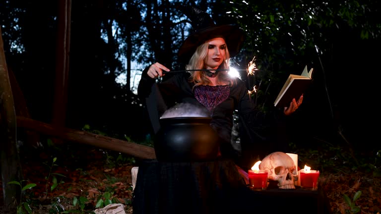 A young witch casting a magic spell in a Halloween ritual with a sparkle wand and white smoke effect in the forest.