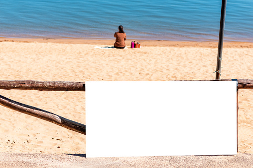 billboard on beach with person sitting on sand with copy space