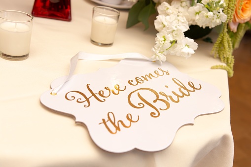 An elegant wedding table setting with a wooden sign featuring 'here comes the bride' placed close to a lit candle