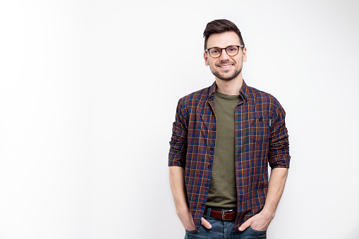 Unshaved charming cheerful positive young man in glasses hold hands pockets isolated on white background
