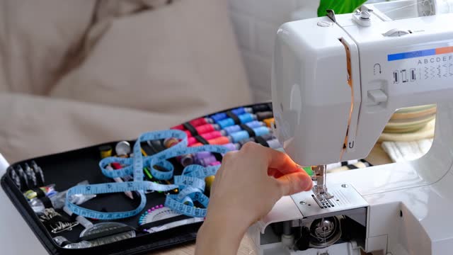 Woman hand close up sews tulle on electric sewing machine. Filling the thread into the sewing needle, adjusting the tension. Comfort in the house, a housewife's hobby, layout of sewing tools
