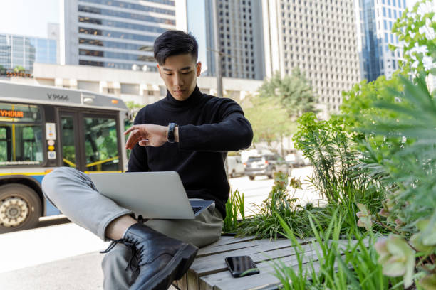 istock Busy asian man sitting using laptop, checking time. Attractive chinese student preparing for exam 1659563733