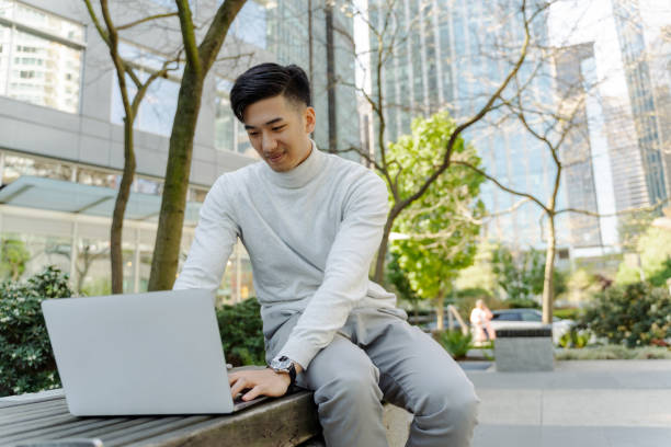 istock Asian man using laptop, sitting on bench outdoors. Chinese businessman working online, remote work 1659564264