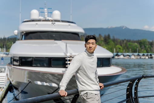 Handsome asian businessman standing near yacht, looking away. Attractive chinese businessman at yacht club, looking away, posing for picture