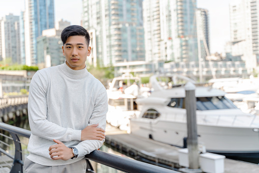 Successful asian businessman standing by yacht in port, looking at camera. Confident chinese man posing for picture. Business concept